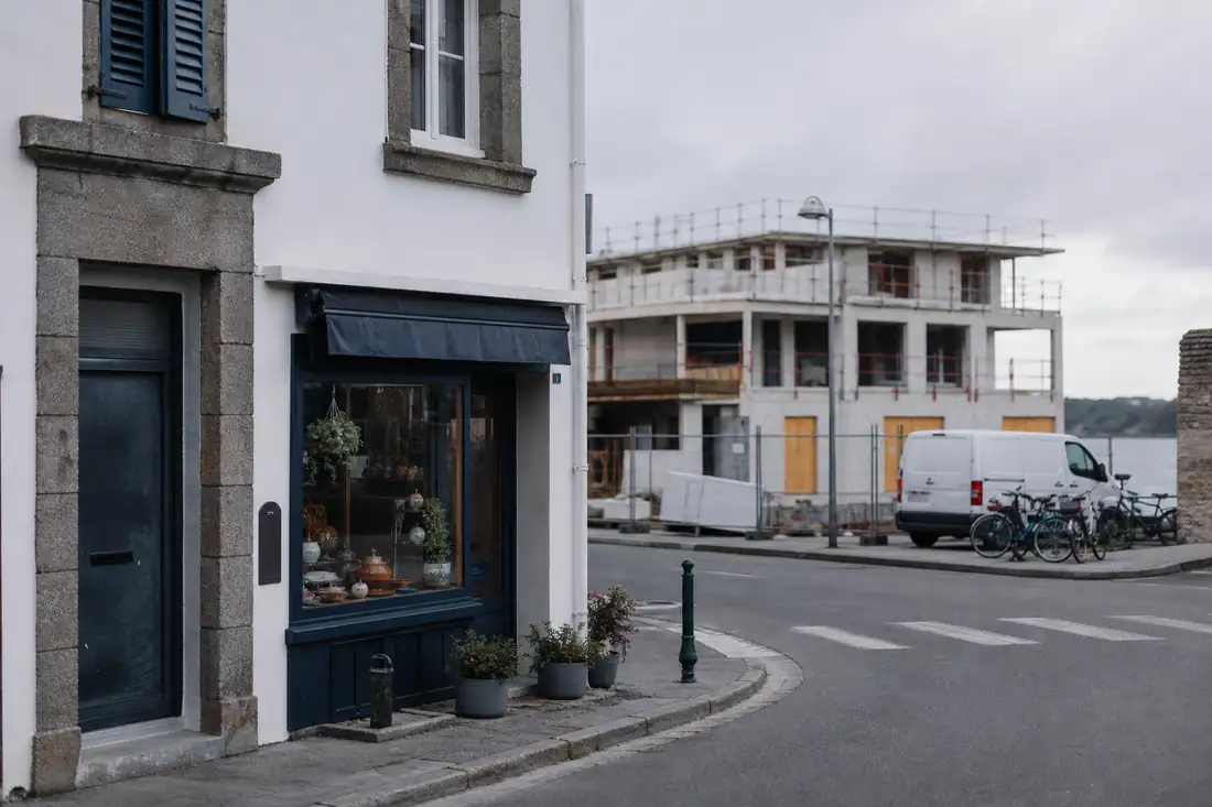 Commerce de proximité face à un chantier immobilier dans une rue de Crozon, avec circulation et vélos.