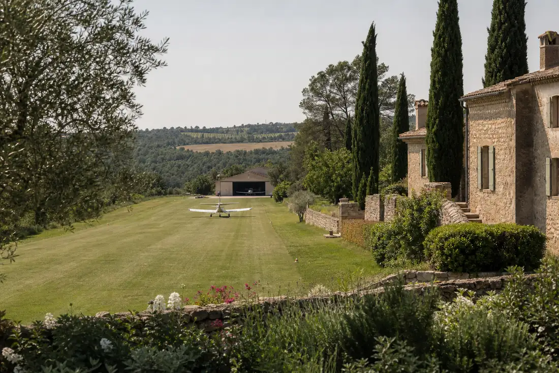 Domaine rural haut de gamme en Occitanie avec piste en herbe bordée d’arbres et hangar discret.