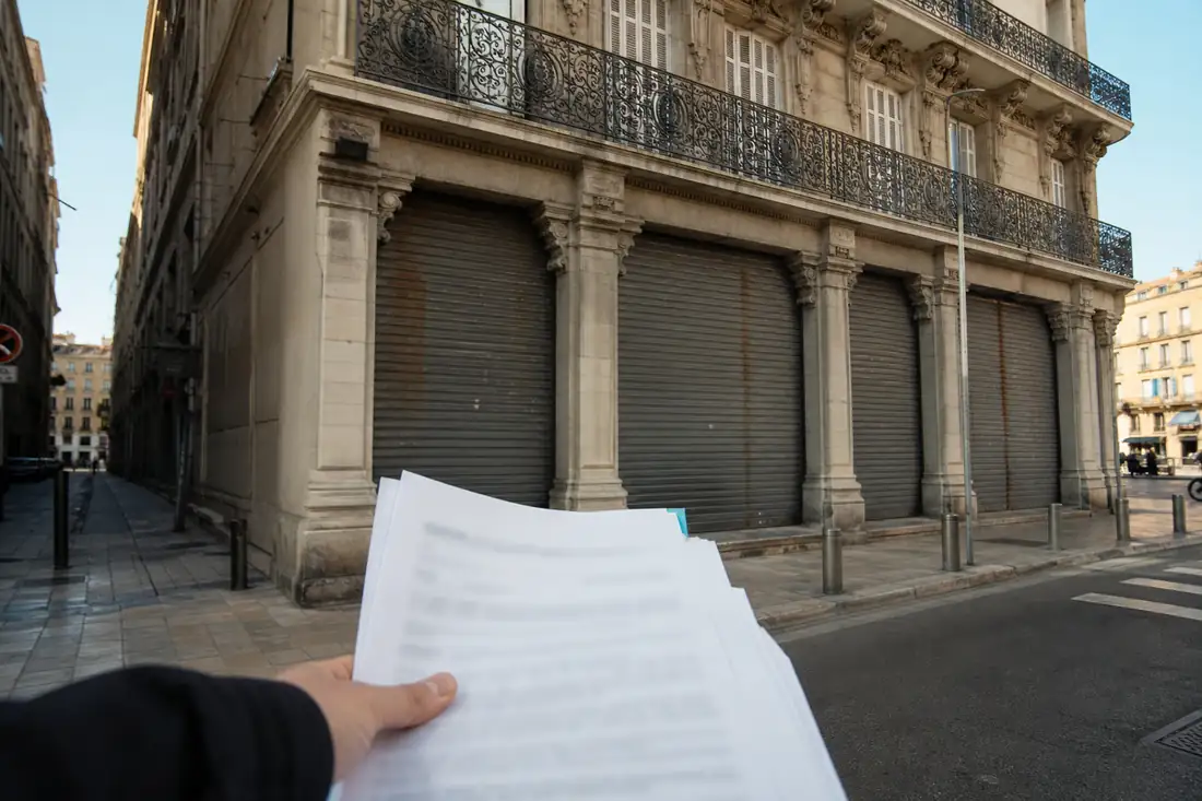 Façade d’un immeuble commercial marseillais devant lequel un dossier de vente aux enchères est consulté.