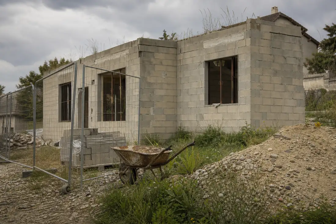 Maison individuelle inachevée sur un chantier à l’arrêt, ouvertures non posées et matériaux laissés sur place