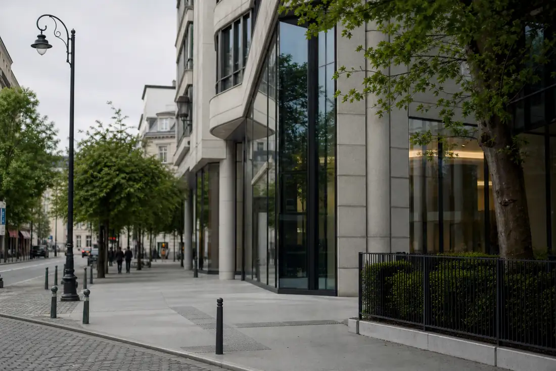 Immeuble de bureaux contemporain à Bruxelles, façade vitrée et quartier tertiaire arboré sous ciel couvert.