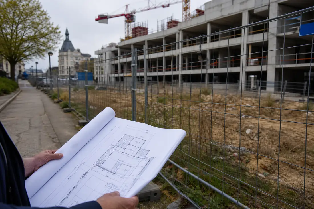Chantier résidentiel interrompu à Argenteuil avec plans d’architecte au premier plan et immeubles urbains en arrière-plan.