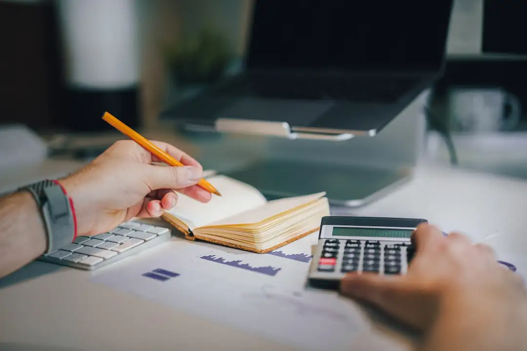 Analyste examinant des documents financiers et plans immobiliers dans un bureau lumineux, face à un immeuble urbain.