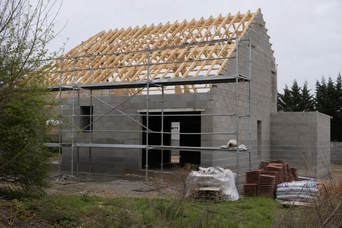 Maison individuelle en cours de construction, murs montés et charpente posée, échafaudage le long de la façade
