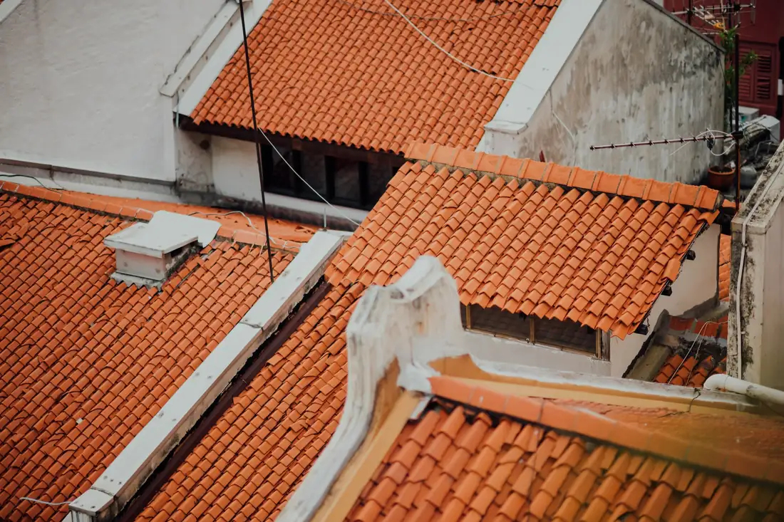Couvreur inspectant le solin d’une cheminée sur une toiture en tuiles avec équipement de sécurité.