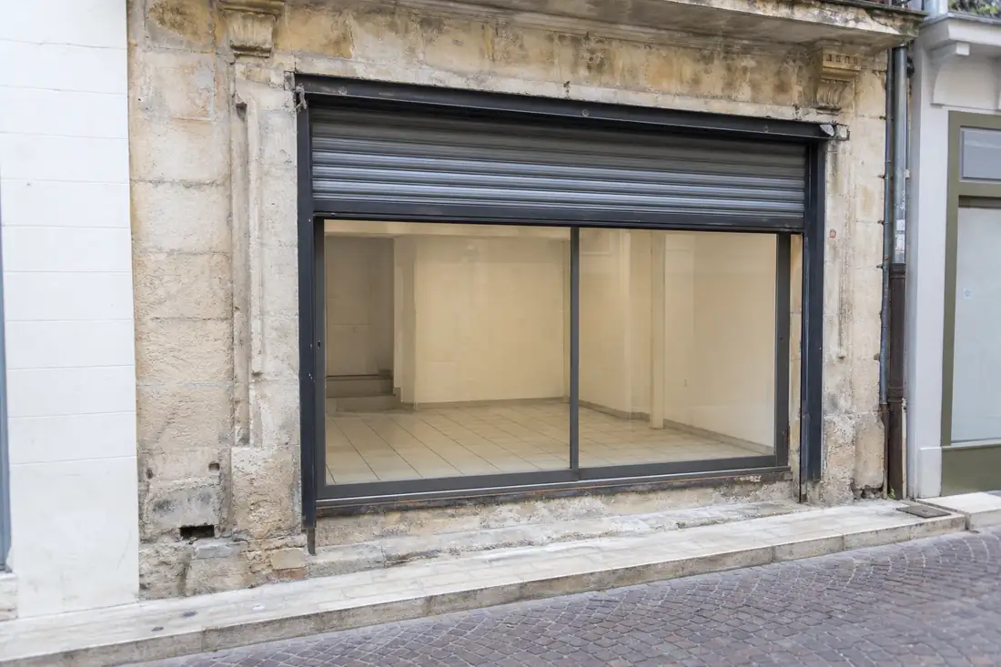 Local commercial vacant en centre-ville, vitrine vide et rideau métallique à demi relevé