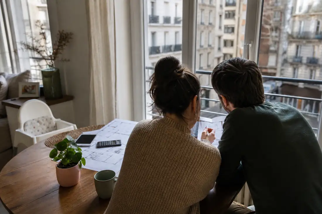 Couple examinant des plans et un budget dans un appartement urbain avant un projet familial.