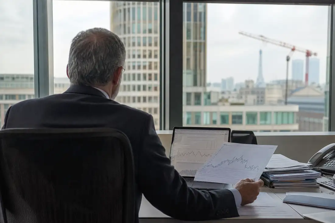 Gestionnaire analysant un portefeuille d’actifs dans un bureau financier face à un quartier de bureaux.
