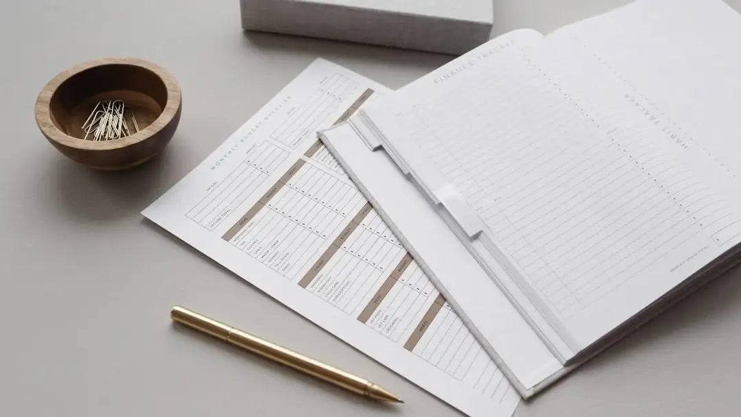 Couple examinant un budget d’achat immobilier avec calculatrice, plans et dossier de financement sur une table.