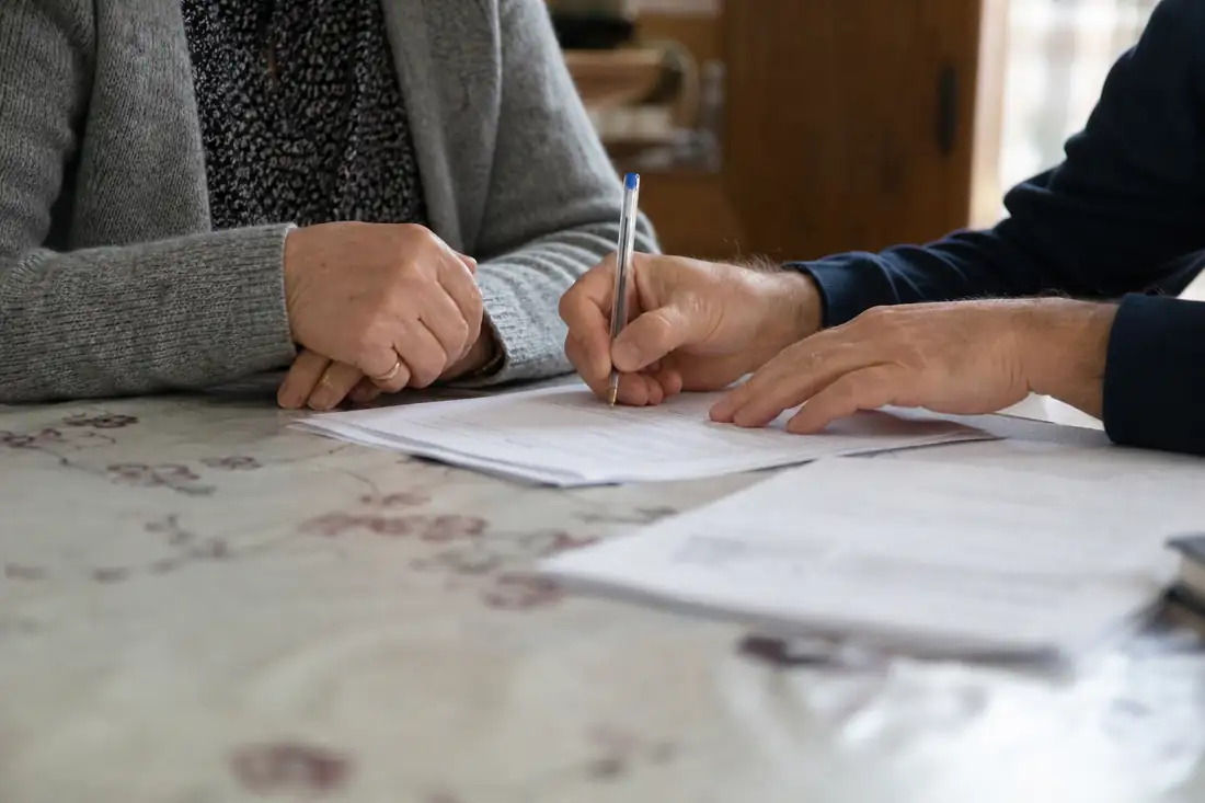 Parent et enfant adulte signant ensemble un document financier à la maison