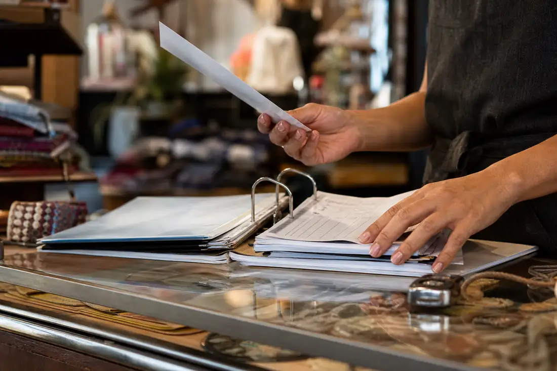 Commerçant consultant un bail et des factures de charges au comptoir de sa boutique