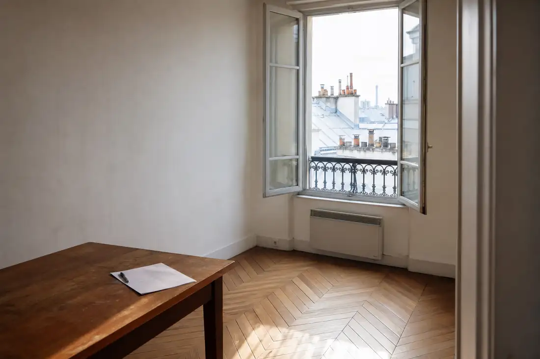Petit appartement parisien vide, fenêtre ouverte sur les toits de zinc et bail posé sur une table en bois