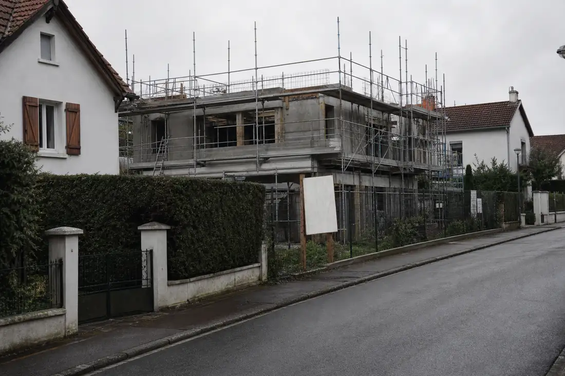 Chantier d’immeuble en cours d’élévation en limite de pavillons, vu depuis la rue d’un quartier résidentiel