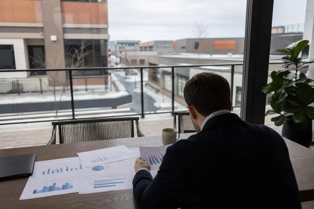 Investisseur consultant des documents financiers devant un ensemble immobilier commercial canadien en lumière naturelle.