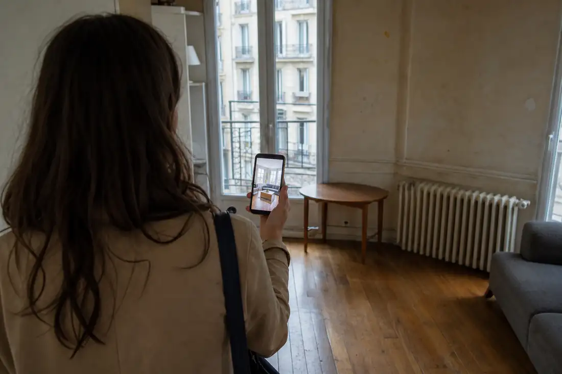 Locataire comparant une annonce sur smartphone avec l’état réel d’un appartement lors d’une visite.