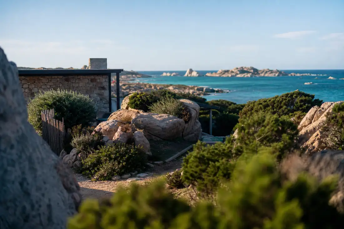 Villa de pierre intégrée aux rochers d’une île corse, avec maquis méditerranéen et mer en arrière-plan.