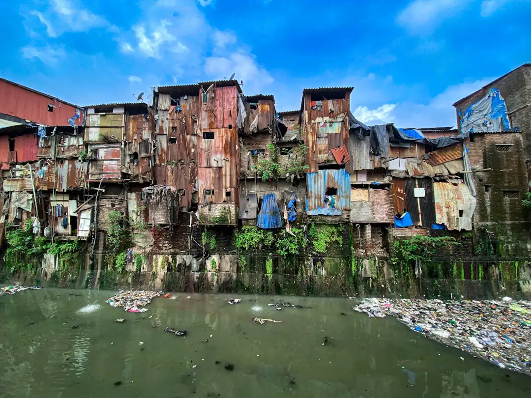 Ruelles denses et ateliers de Dharavi à Mumbai, avec des immeubles récents visibles à l’arrière-plan.