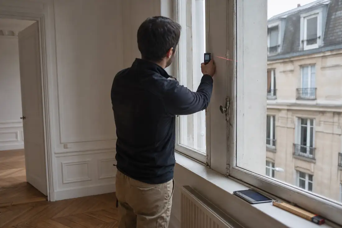 Diagnostiqueur relevant les caractéristiques d’une fenêtre ancienne dans un appartement en cours de vente