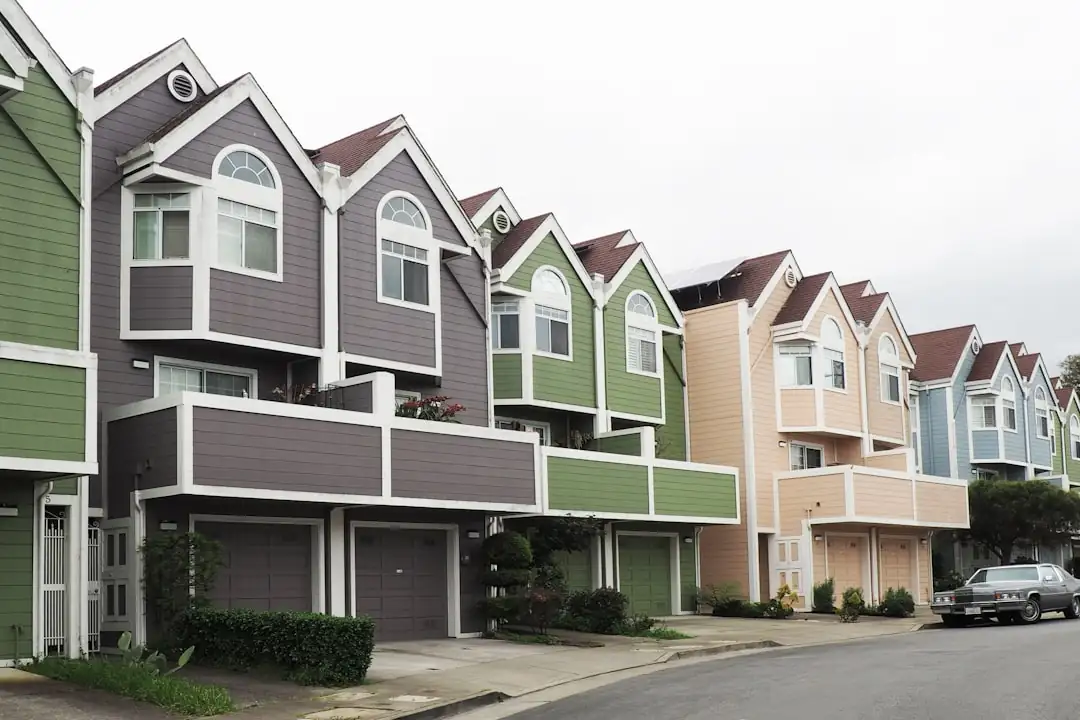 Rue résidentielle américaine au printemps avec maisons individuelles et visiteurs devant une propriété en vente.