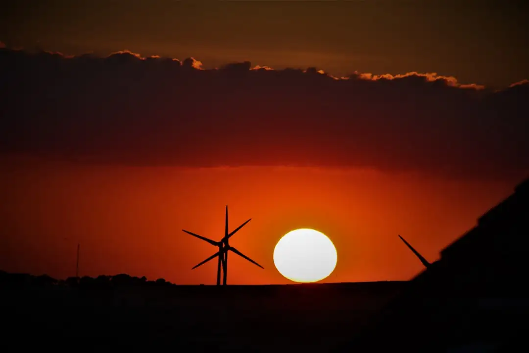 Panneaux photovoltaïques sur la toiture d’un immeuble avec éoliennes visibles au loin dans un paysage périurbain.