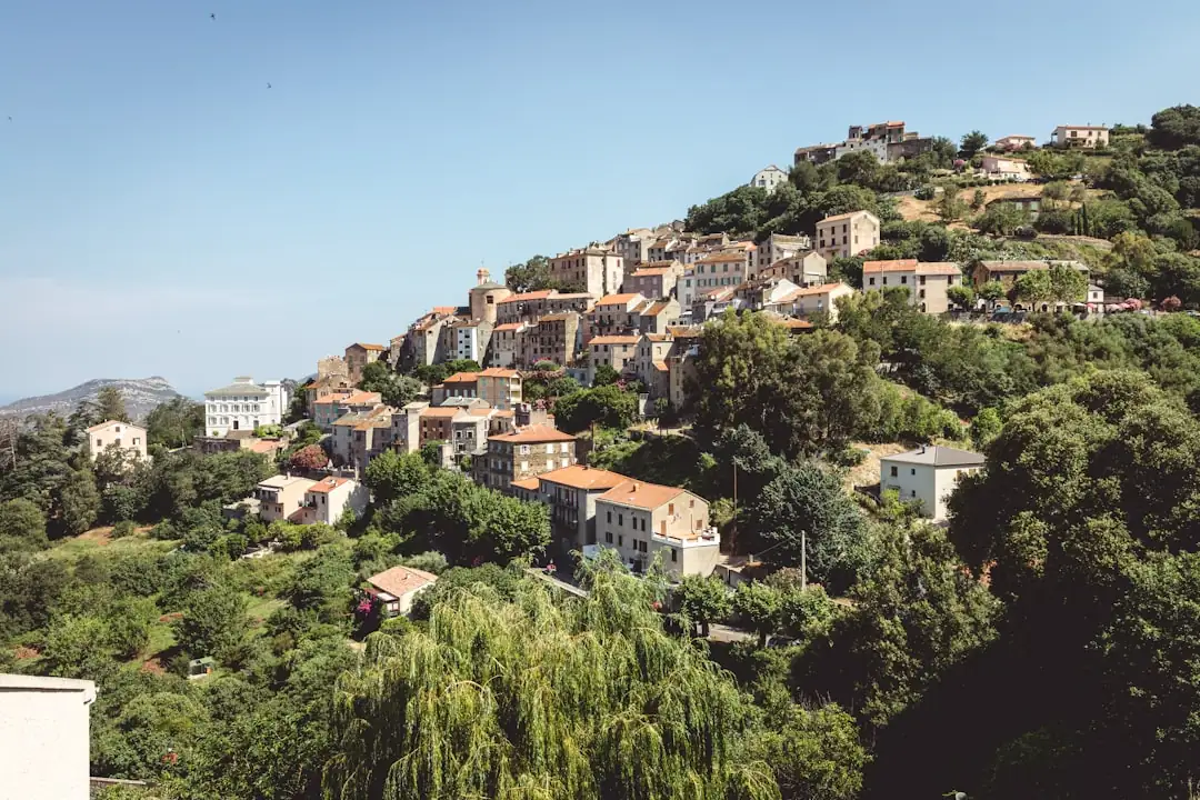 Couple examinant un plan de financement avec un conseiller, devant des maisons corses près du littoral.