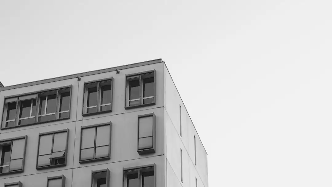 Propriétaire examinant des documents fiscaux non lisibles devant une fenêtre d’appartement en ville.