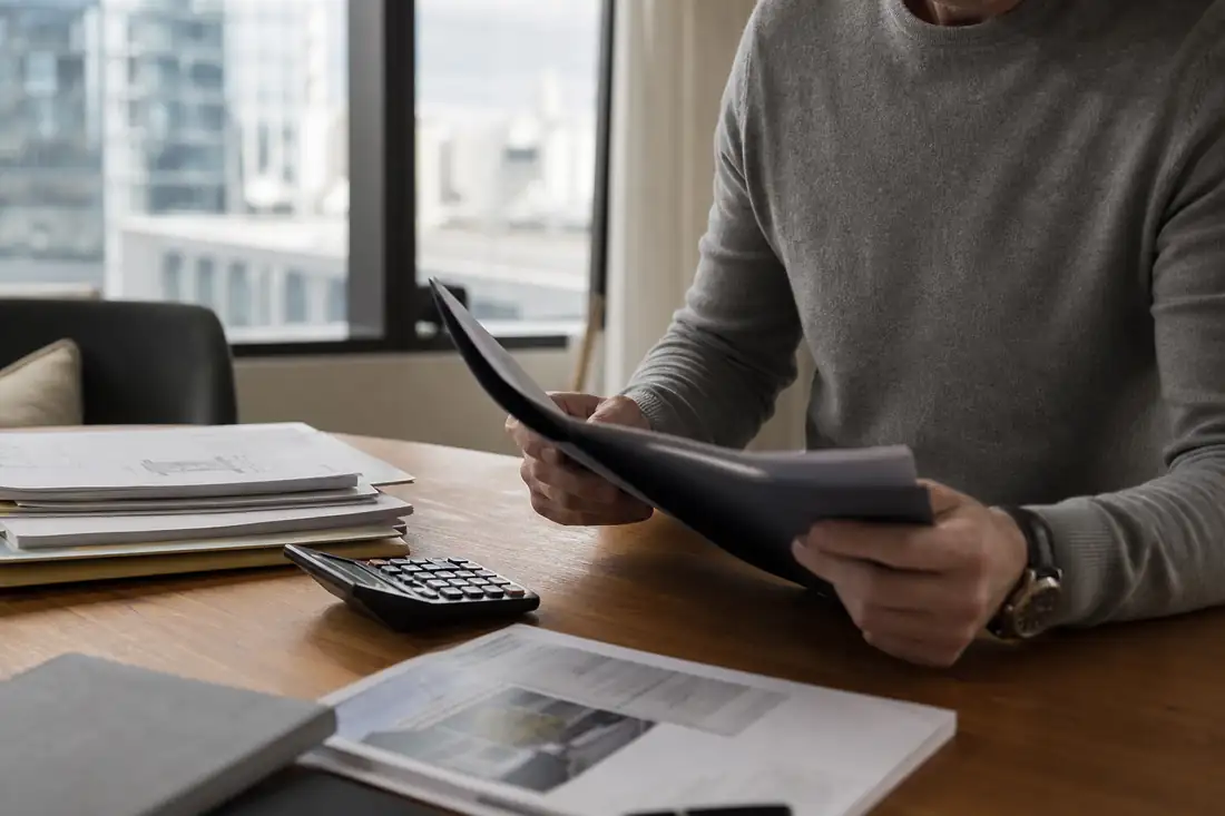 Un épargnant examine un dossier de souscription de SCPI et une calculatrice devant des immeubles de bureaux.