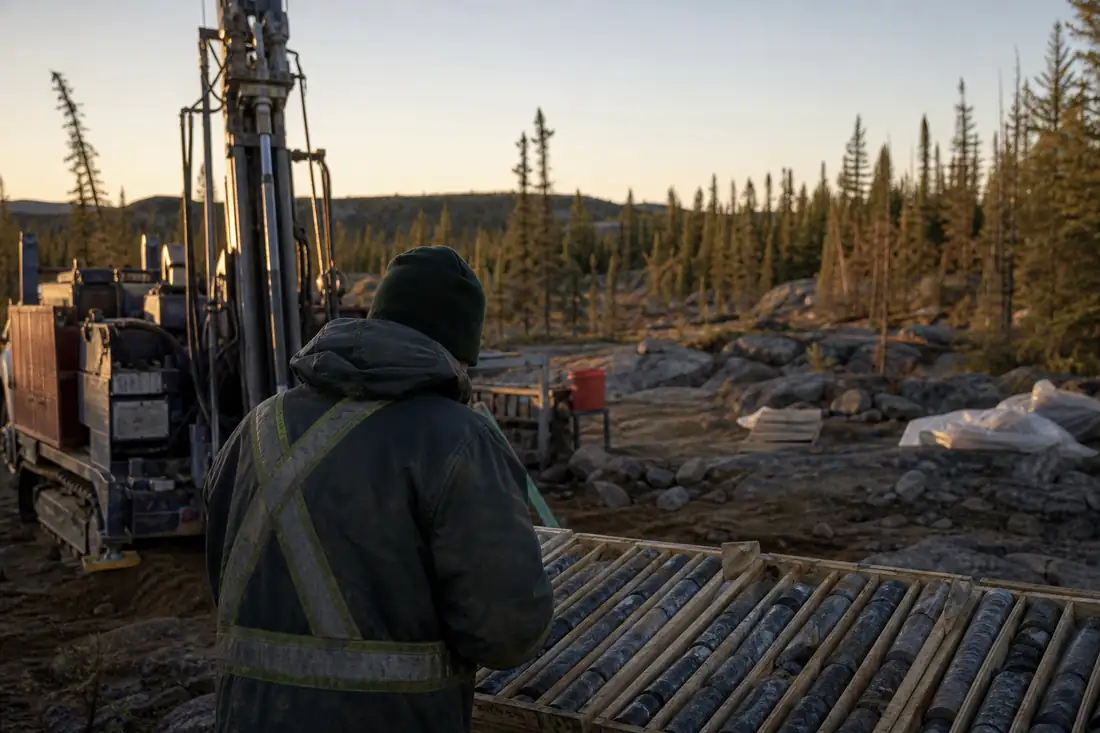 Camp d’exploration aurifère canadien avec carottes de forage et engin de sondage en lisière de forêt.