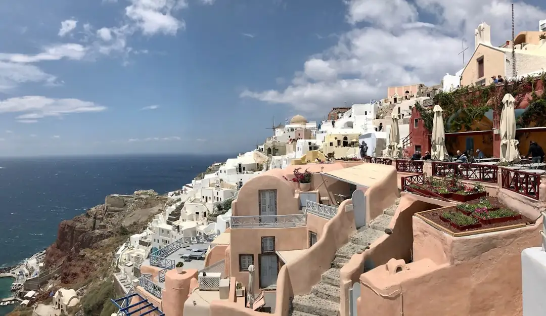 Maison blanche avec terrasse sur une île grecque, face à la mer Égée et à un village méditerranéen.