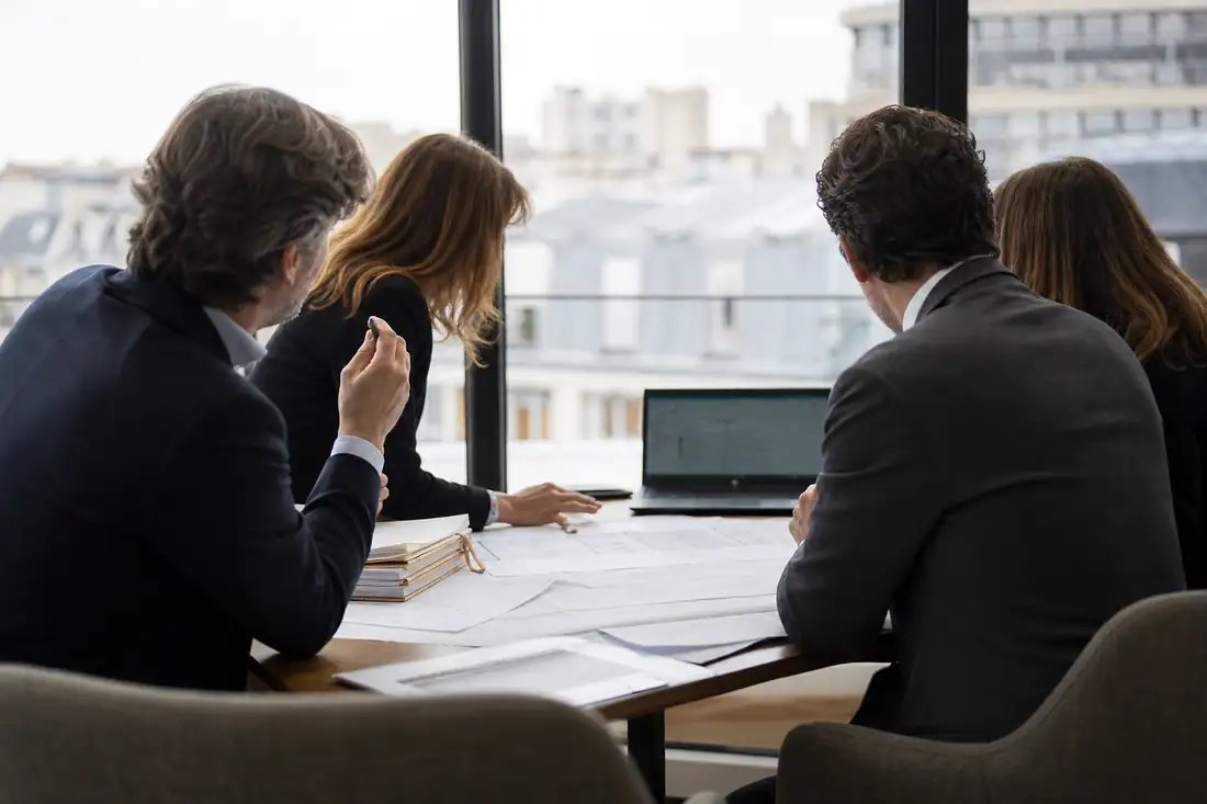 Réunion de direction autour de plans d’immeubles dans un bureau parisien lumineux et sobre