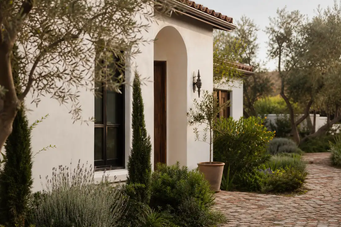Façade rénovée d’une maison californienne aux murs clairs, boiseries sombres et jardin méditerranéen.