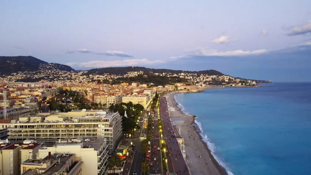 Façades d’immeubles résidentiels niçois avec balcons, acheteur de dos et lumière méditerranéenne.