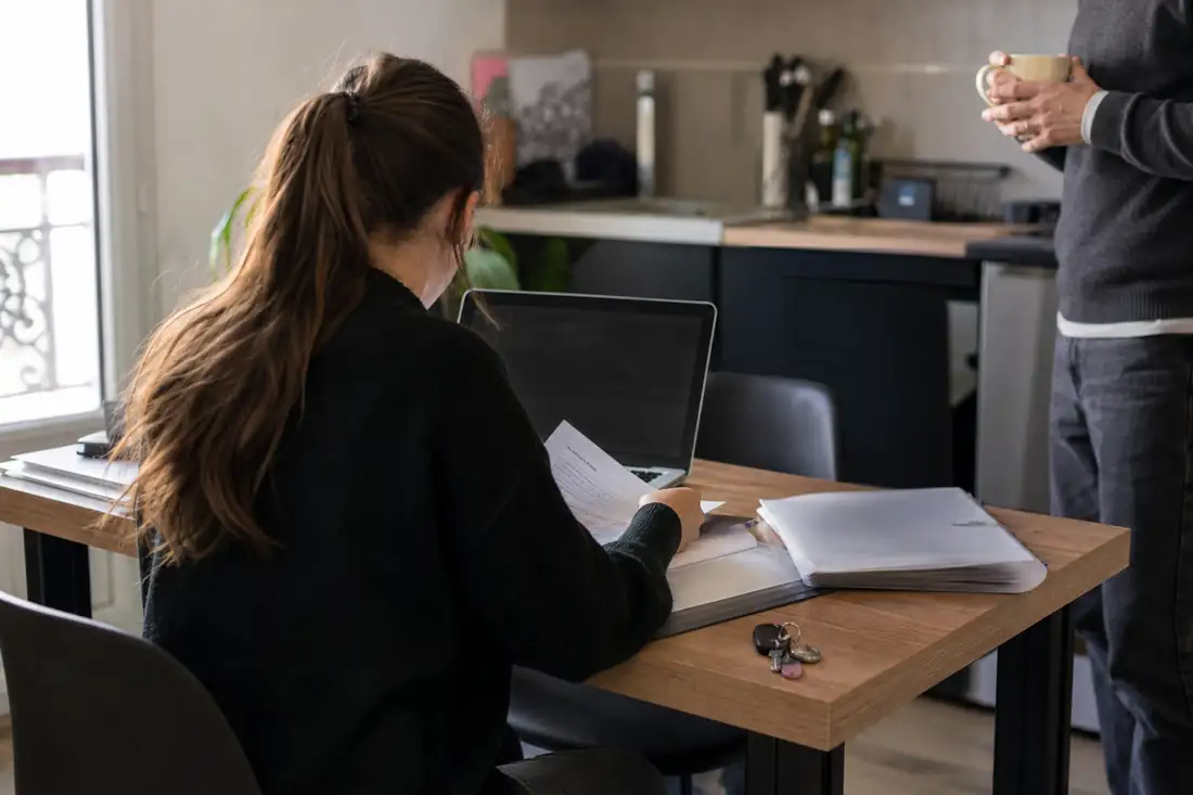 Étudiant préparant un dossier de location avec documents classés et ordinateur dans un appartement meublé.