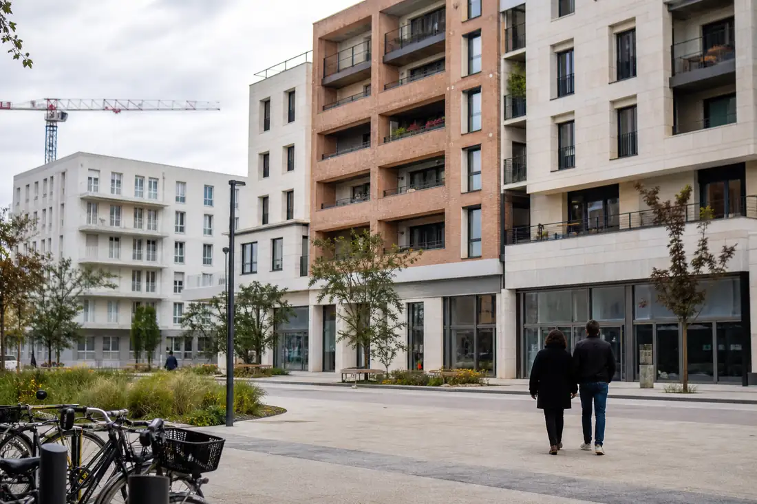 Quartier français en transformation mêlant logements collectifs, commerces de proximité, vélos et espace public végétalisé.