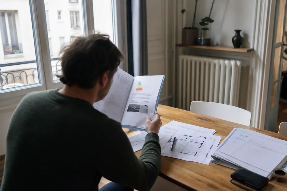 Propriétaire examinant un dossier de DPE et des factures de rénovation dans un appartement ancien.