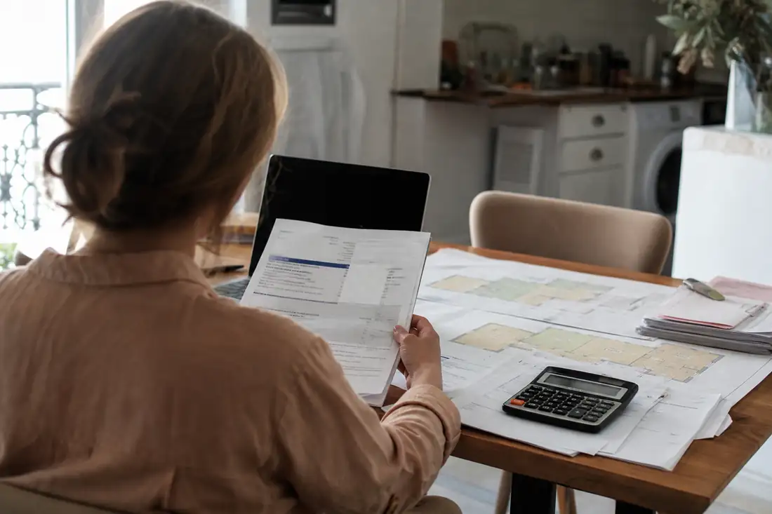 Propriétaire examinant un avis de taxe foncière, des plans cadastraux et des factures de travaux à domicile.
