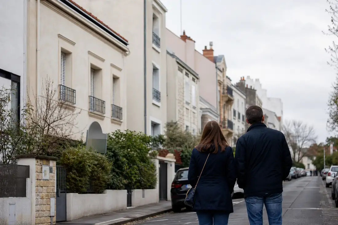 Quartier résidentiel français avec immeubles anciens et maisons, observé par deux visiteurs de dos.