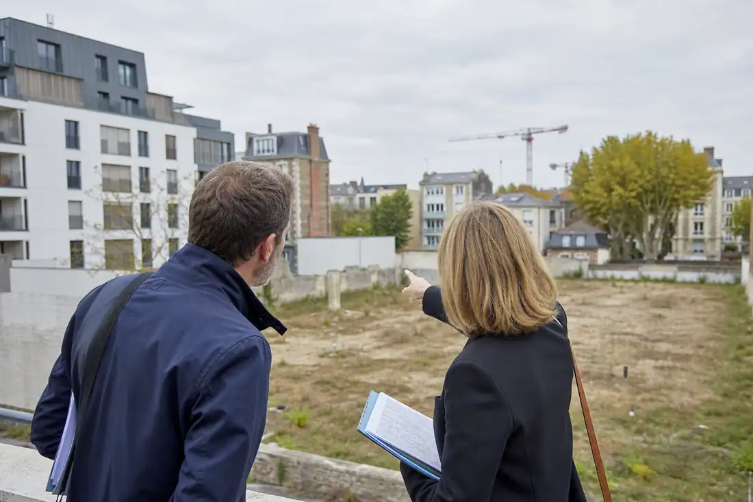 Élus et urbanistes examinant une friche urbaine bordée de logements et d’arbres dans une ville française.