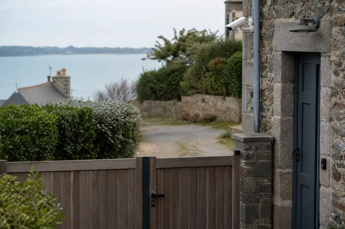 Caméra discrète orientée vers le portail privé d’une maison en pierre du littoral à Cancale.