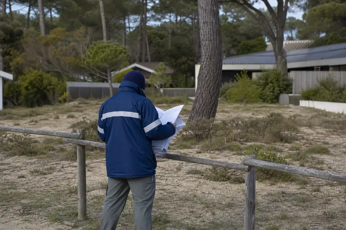 Parcelle littorale arborée du Cap Ferret, clôturée, avec pins maritimes et habitat discret en arrière-plan.