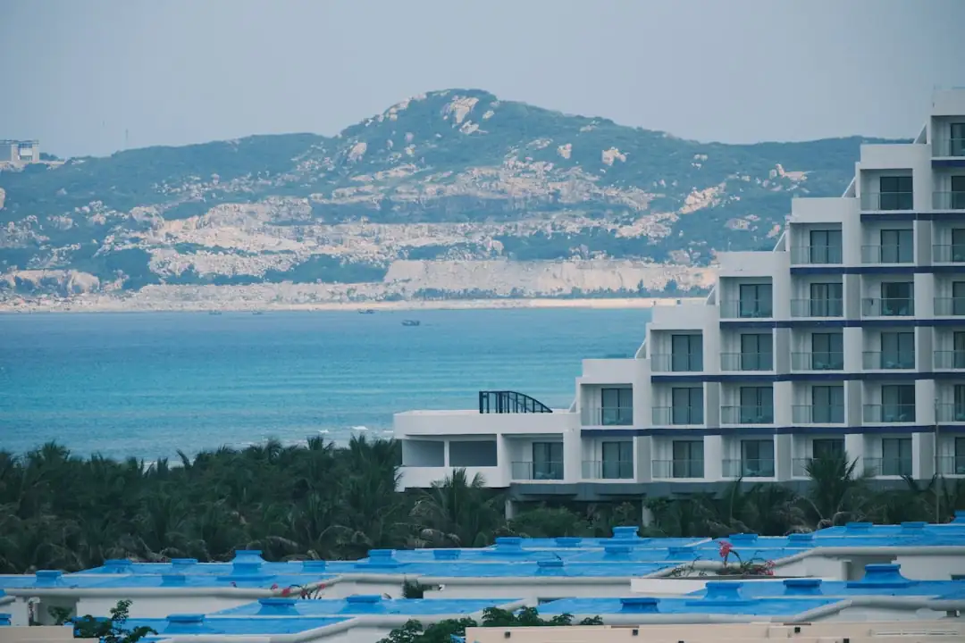 Littoral albanais rocheux avec chantier hôtelier discret et techniciens examinant les contraintes du site.