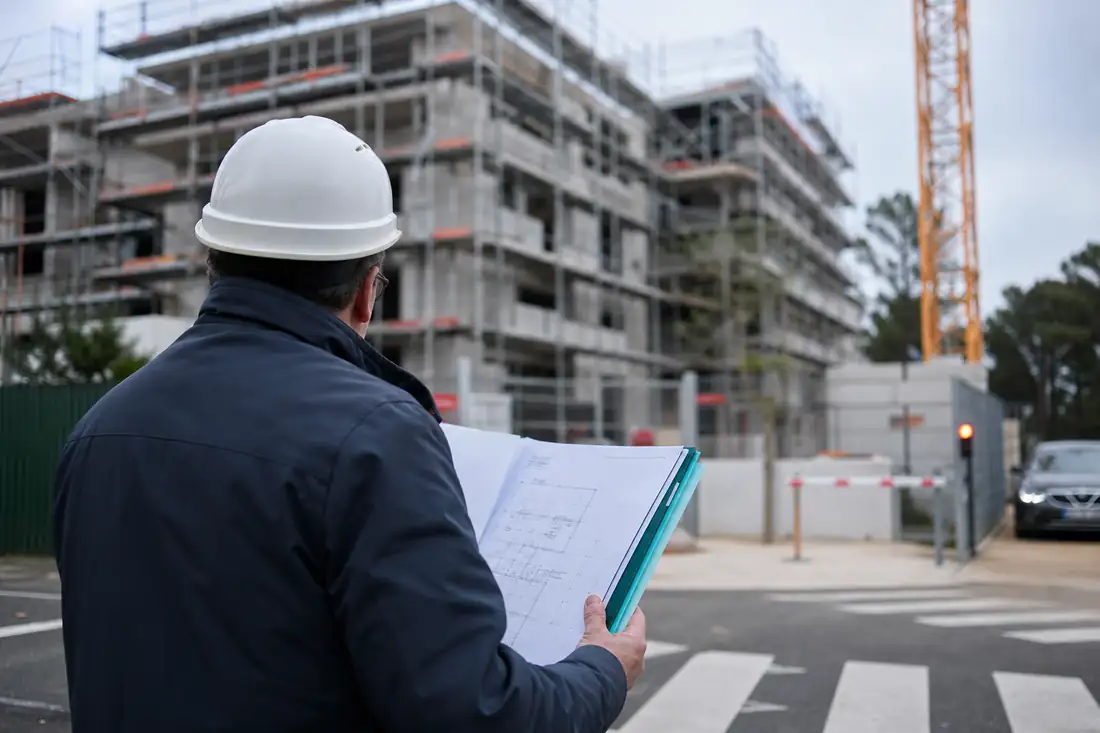 Chantier résidentiel en cours avec plans de construction et dossier juridique au premier plan, dans le Béarn.