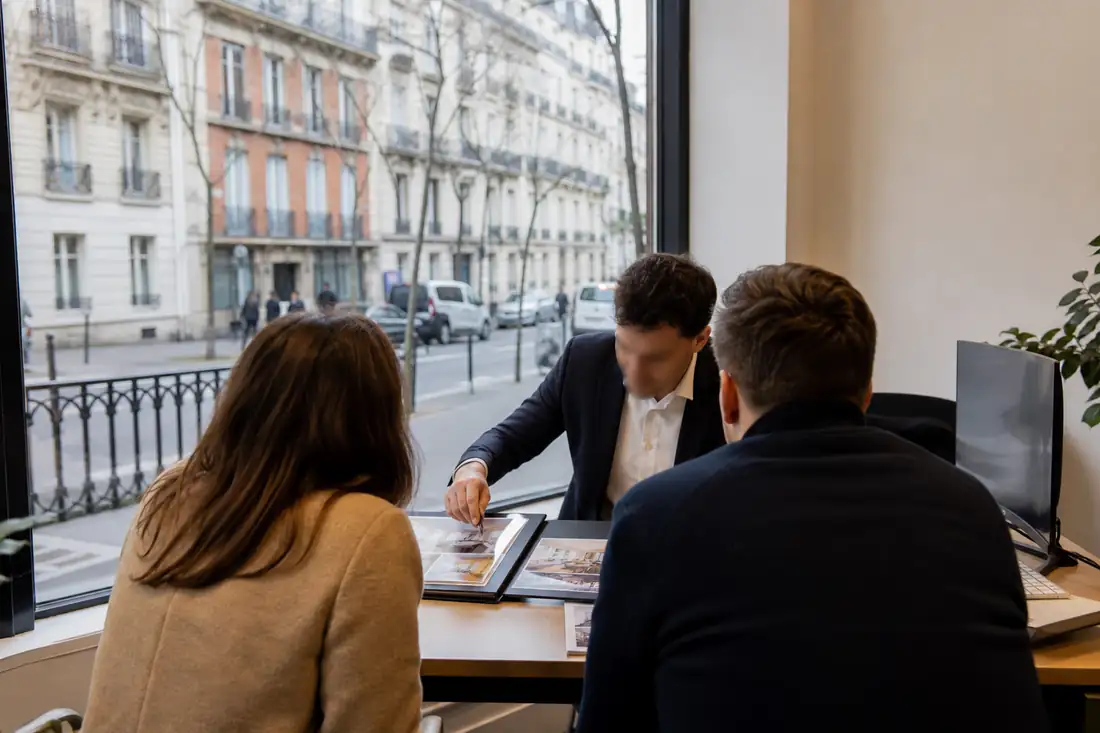 Acquéreurs de dos échangeant avec une conseillère dans une agence immobilière lumineuse en ville.