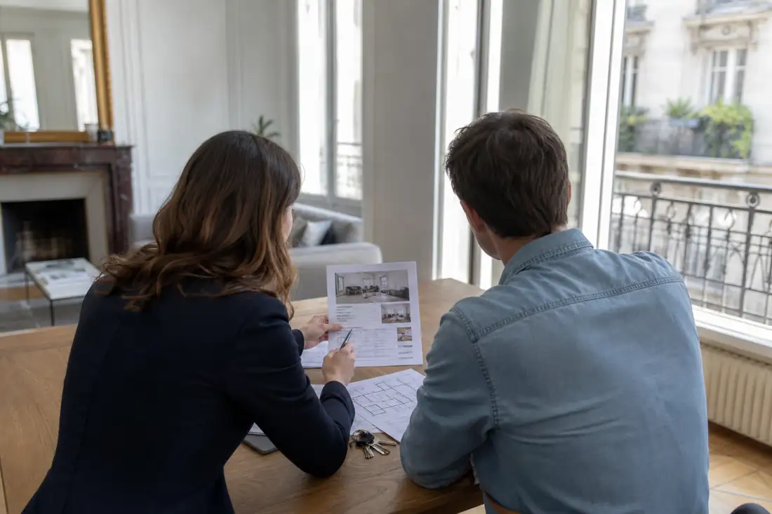 Agent immobilier et propriétaire examinent une estimation de vente dans un appartement lumineux.