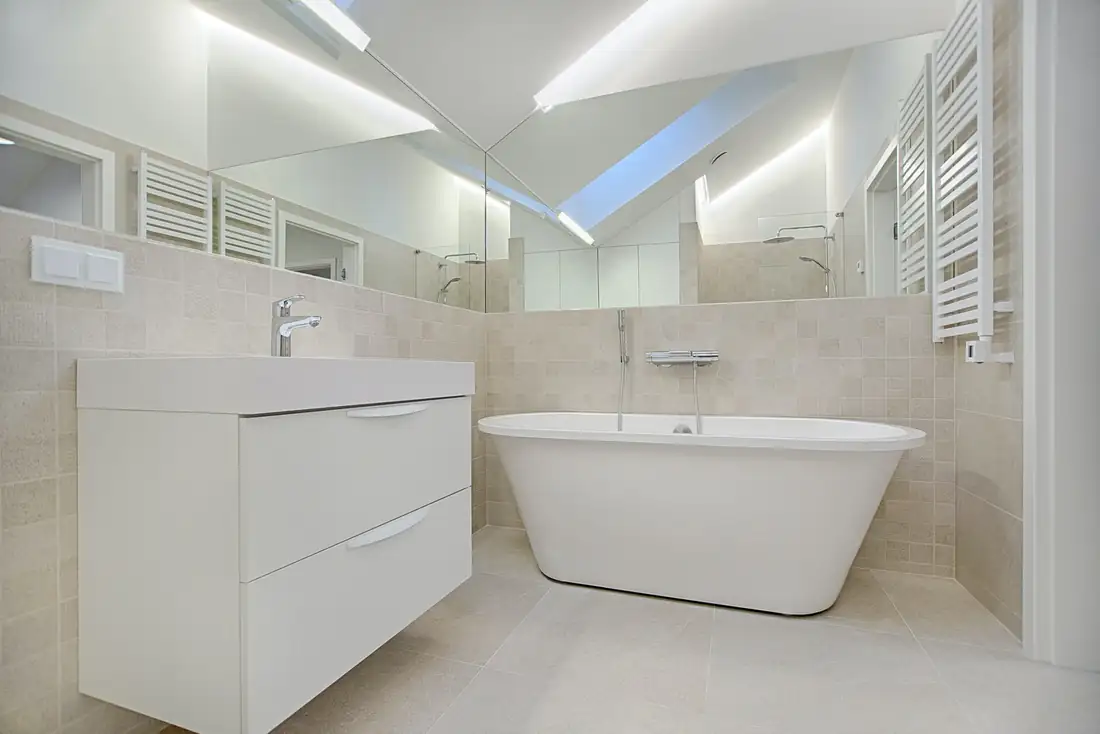 Salle de bain claire avec murs blanc cassé, carrelage beige, meuble en bois clair et grand miroir éclairé.