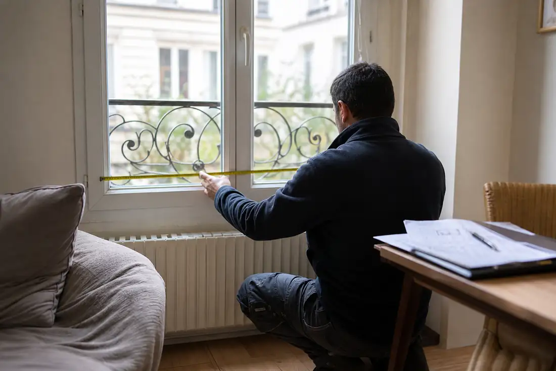 Diagnostiqueur examinant une fenêtre et un radiateur lors d’une visite DPE dans un appartement français.
