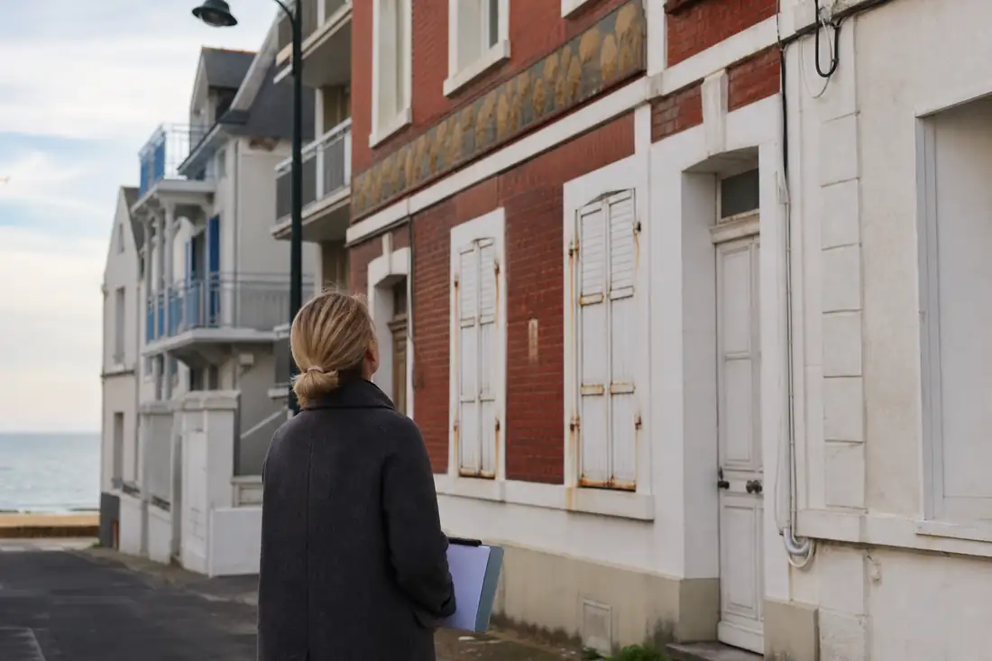 Rue résidentielle près du littoral avec immeubles, maisons rénovées et aperçu de la mer entre les façades.