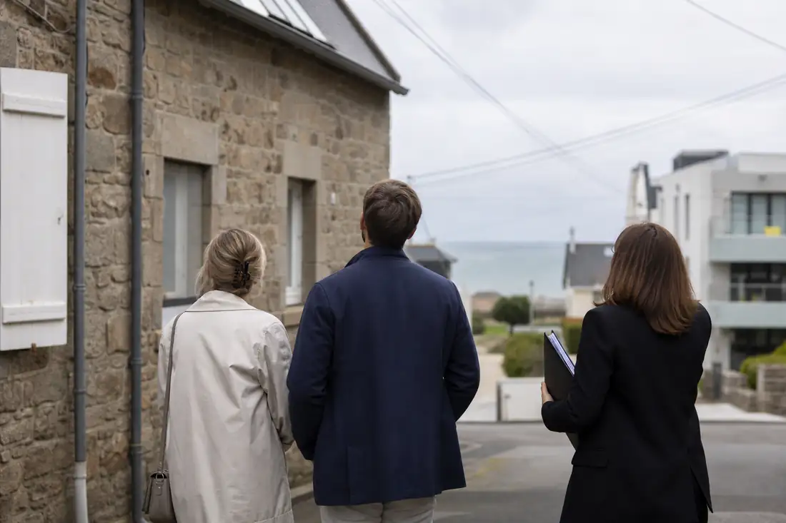 Rue résidentielle bretonne mêlant maisons en pierre et immeubles récents, visitée par des acheteurs potentiels.