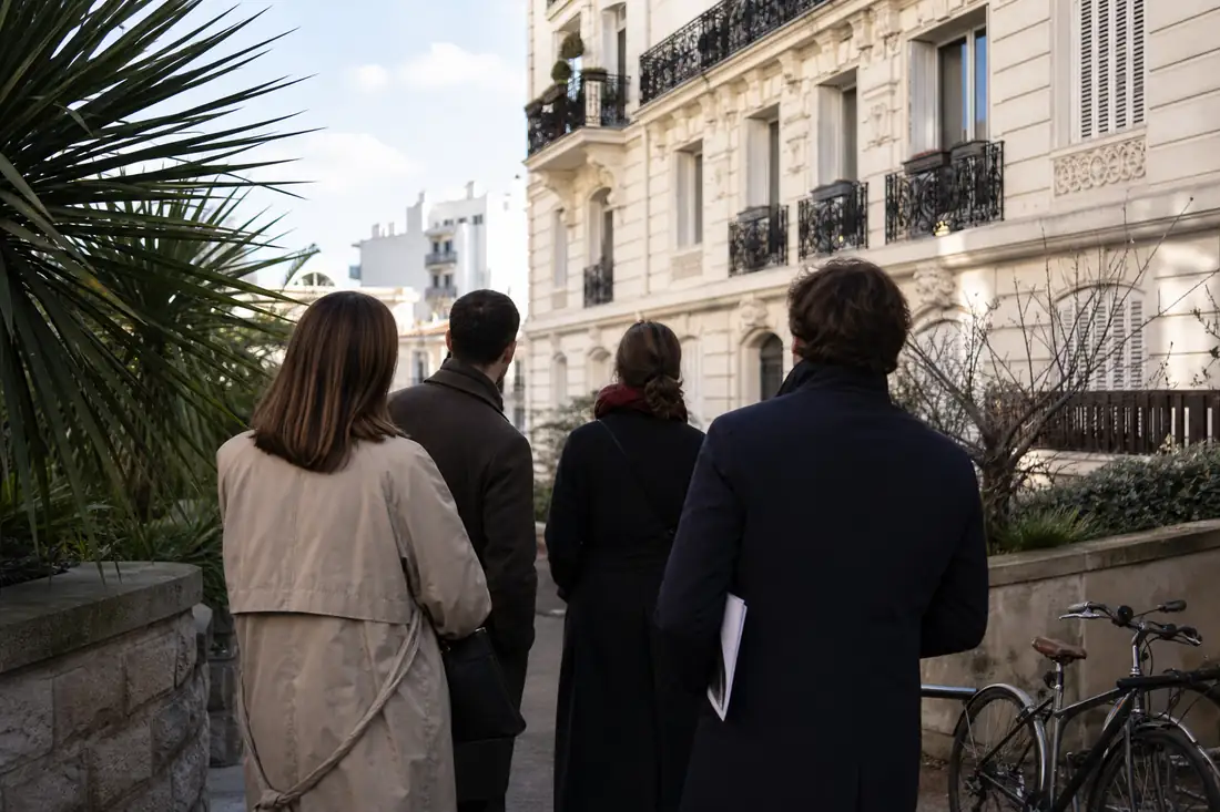 Rue résidentielle d’une ville côtière française avec immeubles anciens et visiteurs devant une agence immobilière.