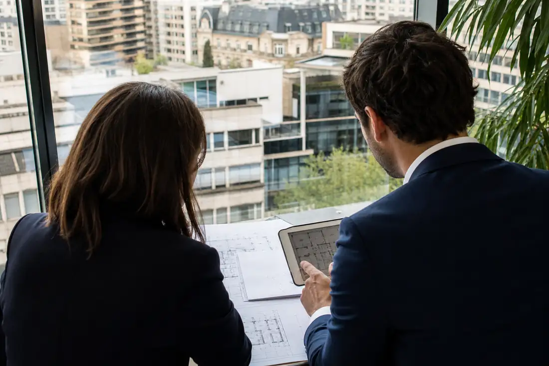 Deux professionnels examinent des plans d’immeubles dans un bureau de conseil immobilier à Paris.